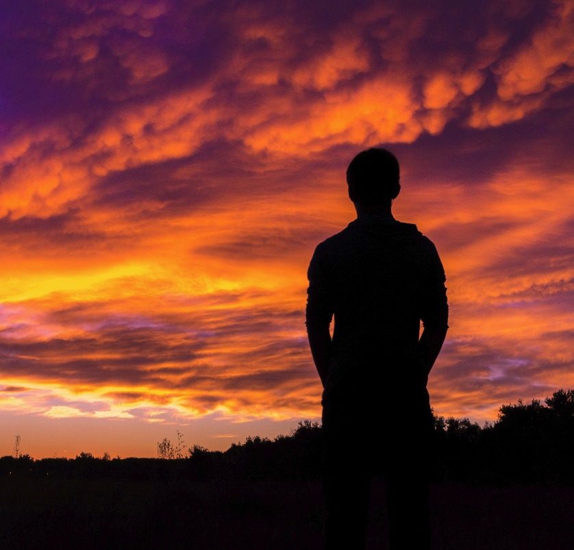 Silhouette of a man against a vivid orange sunset sky